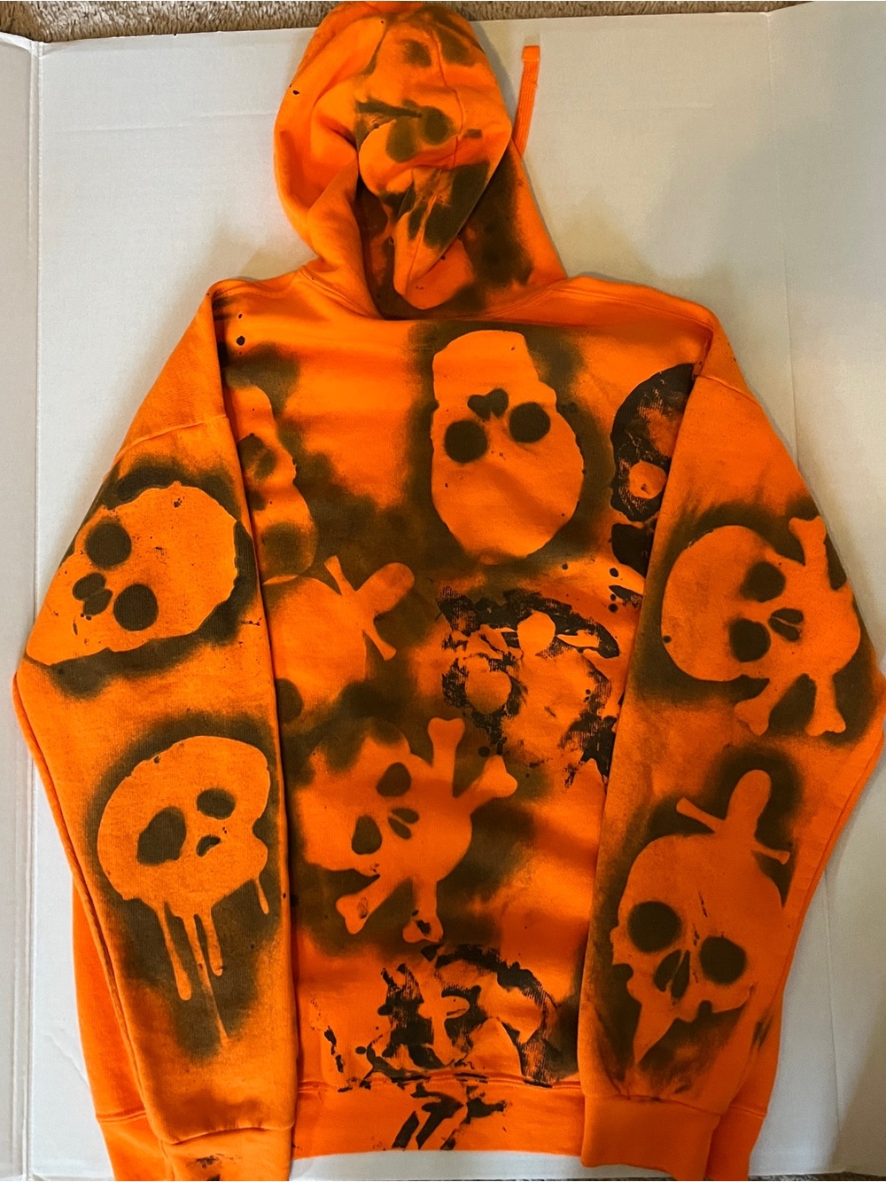 Custom designed orange hoodie featuring black spray-painted skull graphics